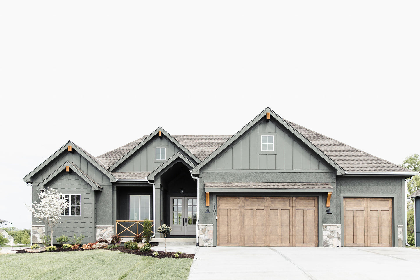 Front view of a craftsman style of architecture custom home with front lawn and landscaping.