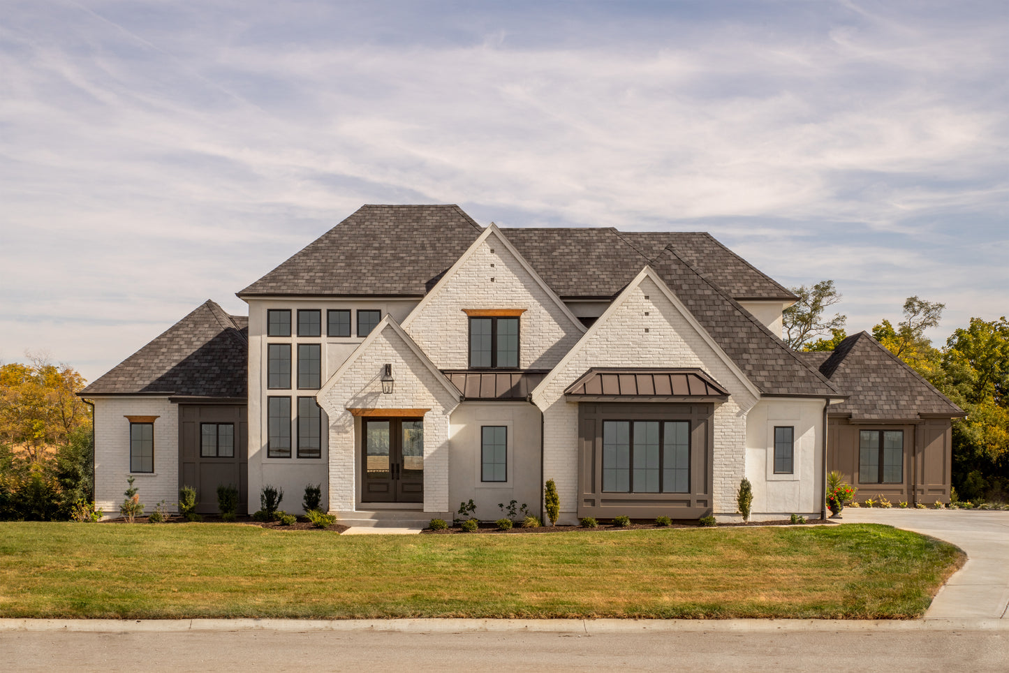 Front of a custom home in the European and Cottage style of architecture with front lawn and landscaping.