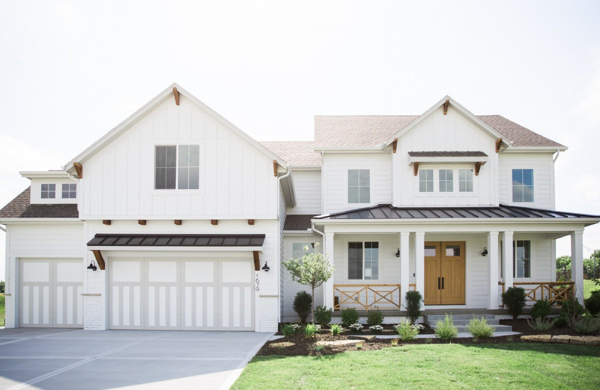 A front elevation of a white home in the farmhouse and craftsman style of architecture with landscaping and green lawn.