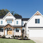 A view of the front of a white home in the farmhouse style of architecture with landscaping and a green lawn.