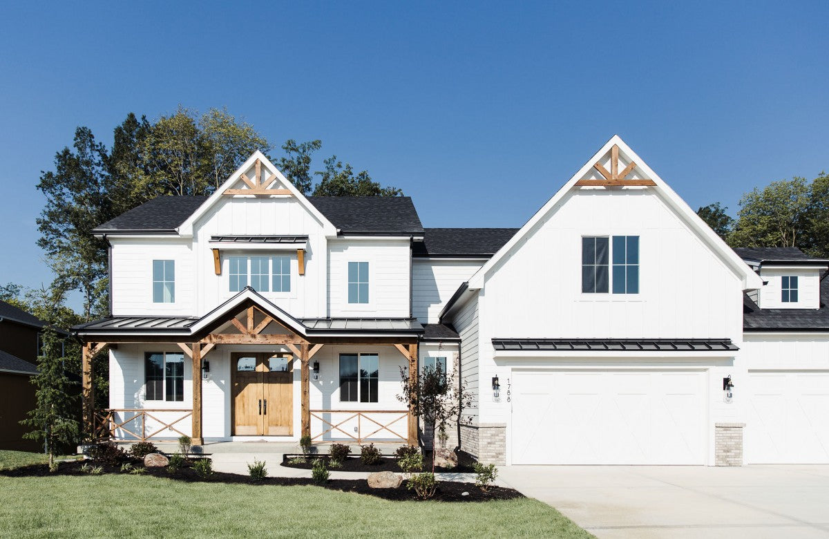 A view of the front of a white home in the farmhouse style of architecture with landscaping and a green lawn.
