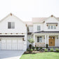 A front elevation of a white home in the farmhouse and craftsman style of architecture with landscaping and green lawn.